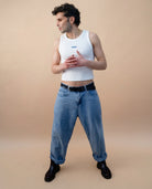 Model wearing a white Biweekly tank top with blue ‘Phase’ text that is crossed out, full body shot front view against a beige background