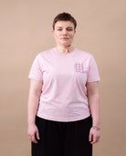 Model wearing light pink Biweekly T-shirt with clit graphic print on right chest area, front view, against beige background