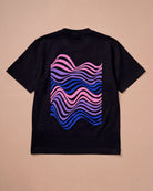 Oversized black Biweekly T-shirt with wavy bi pride flag graphic print and `Perfectly Not Straight` text on the wave print, back view, laying flat on a beige background