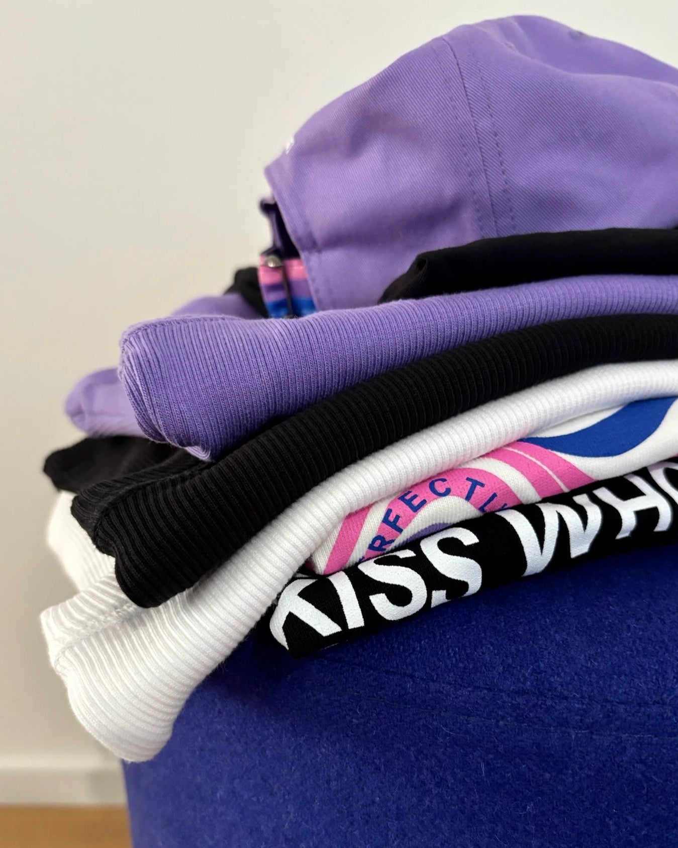 Detail shot of Biweekly clothes stacked on top of each other on a blue stool against white background
