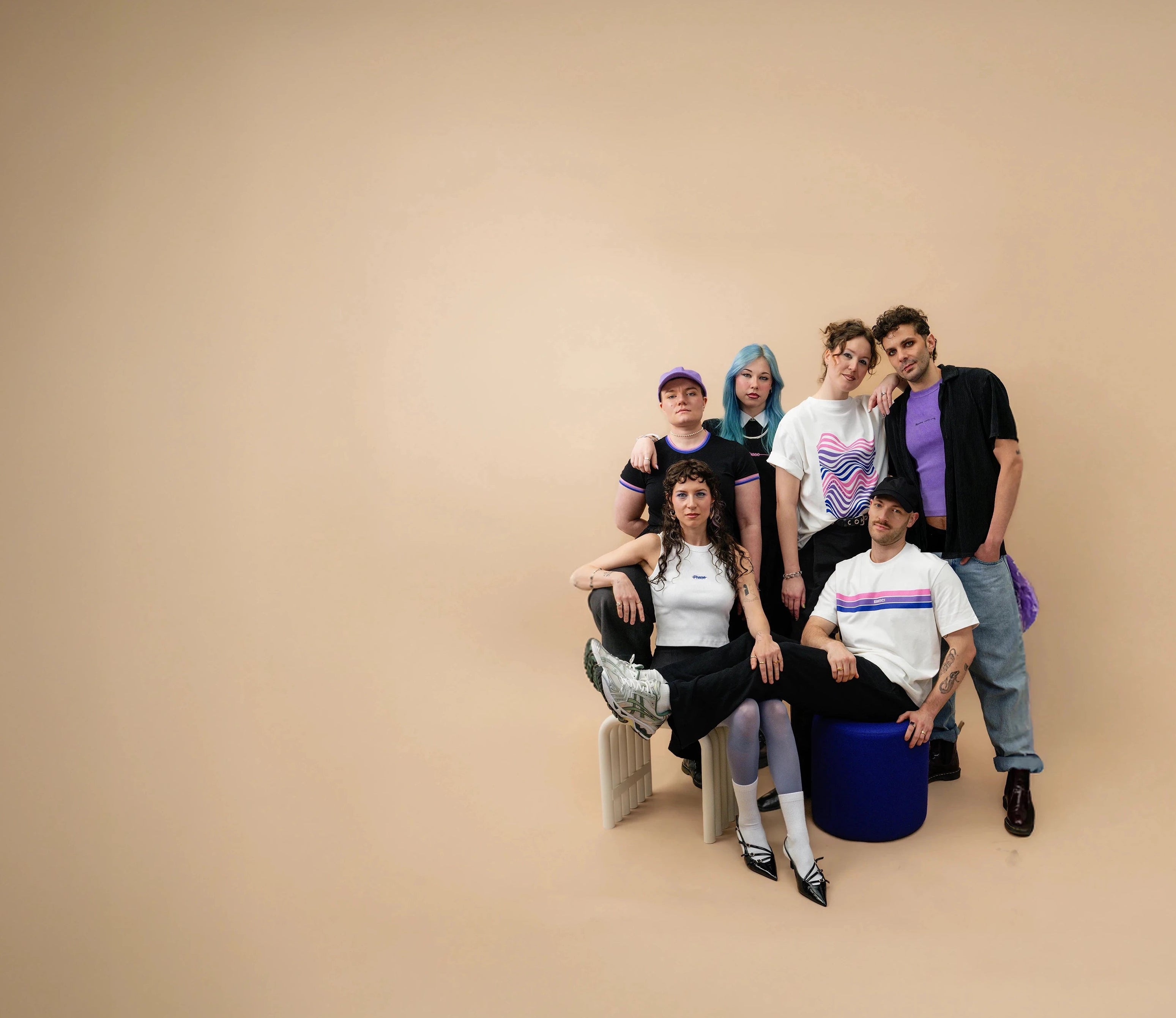 Group of diverse models wearing Biweekly clothing with graphic prints and bi pride color accents, posing together against a beige background
