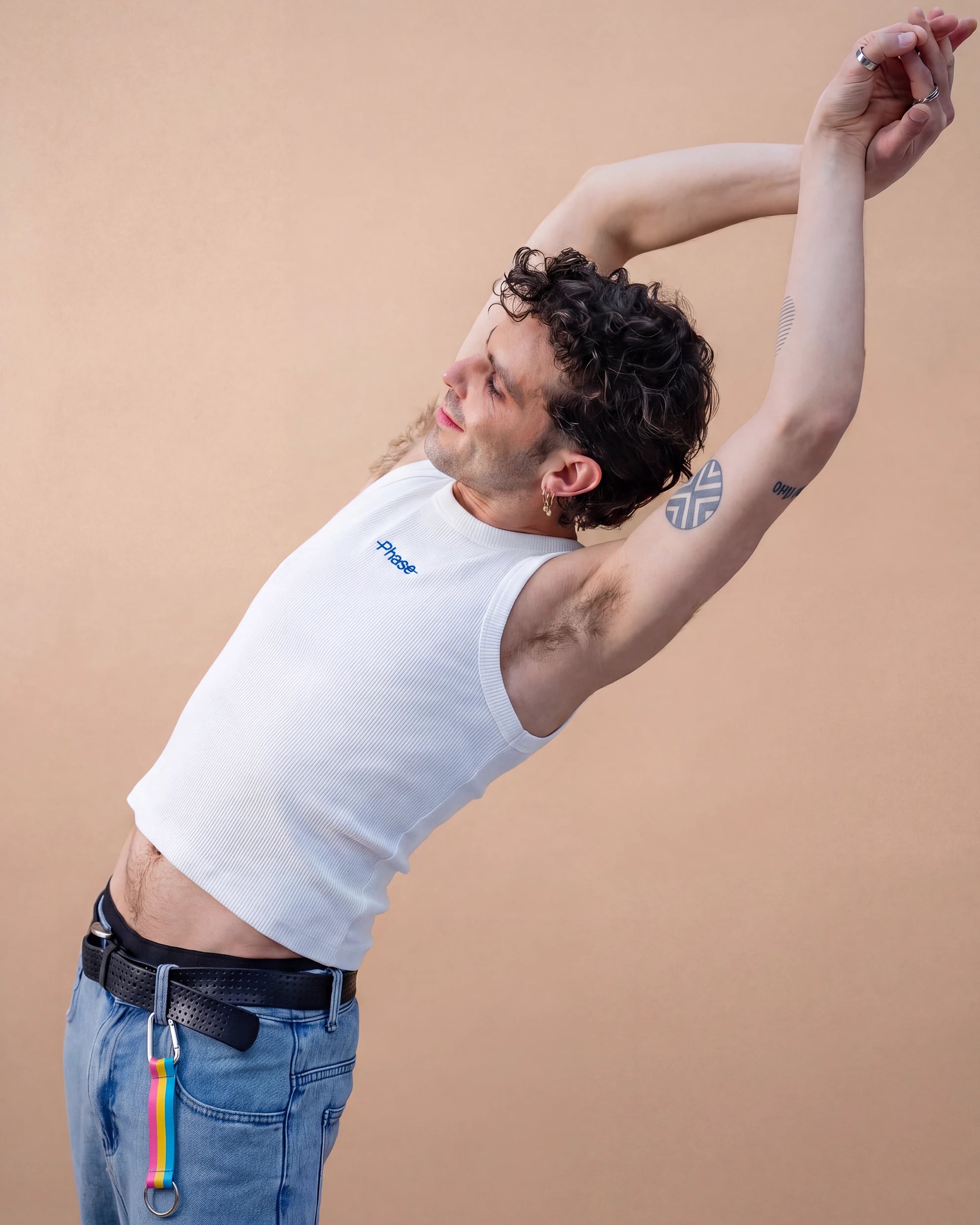 Model wears Biweekly keychain in pan pride flag colors with silver carabiner and blue yarn on his belt loop against beige background