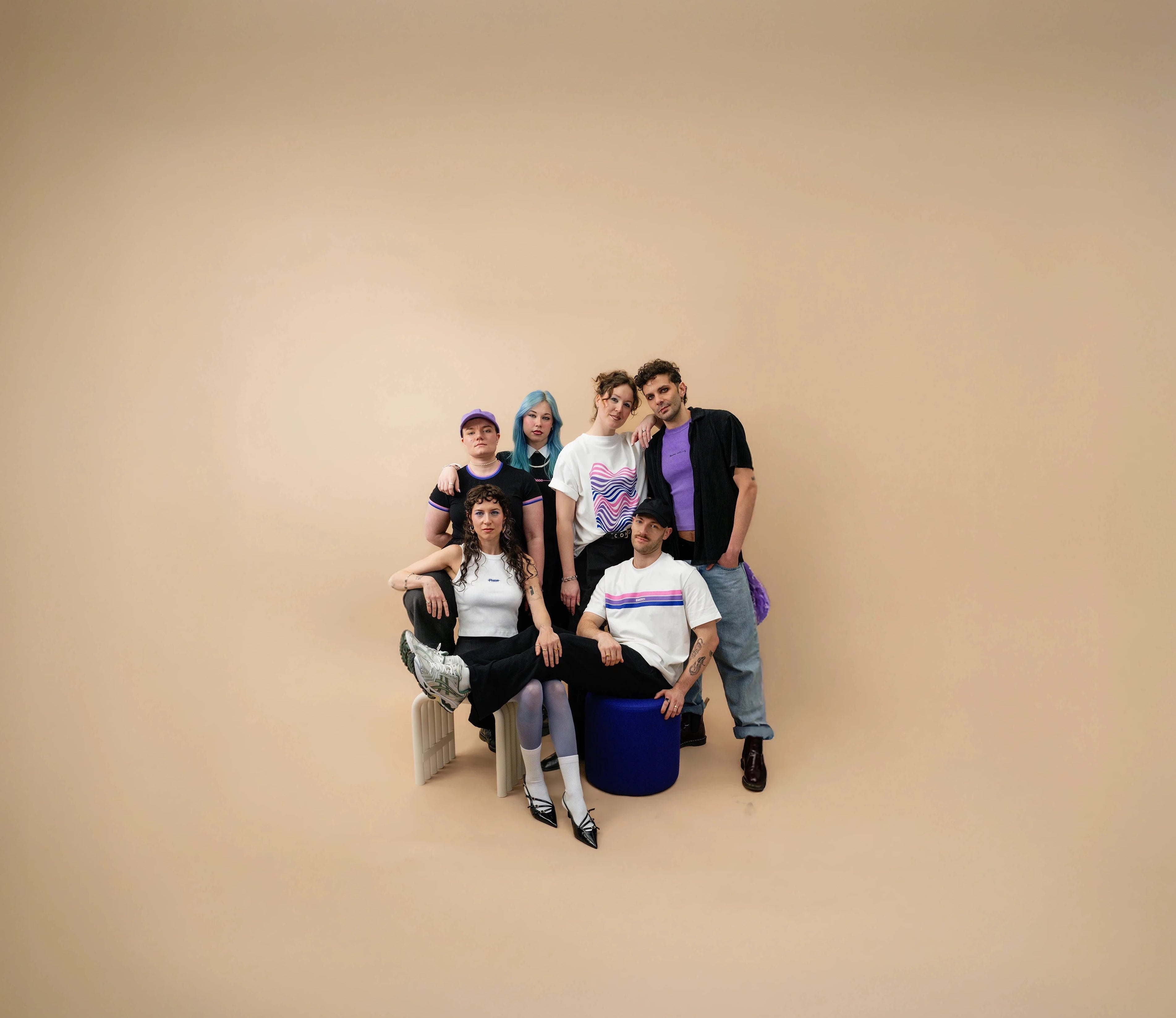 Group of diverse models wearing Biweekly clothing with graphic prints and bi pride color accents, posing together against a beige background