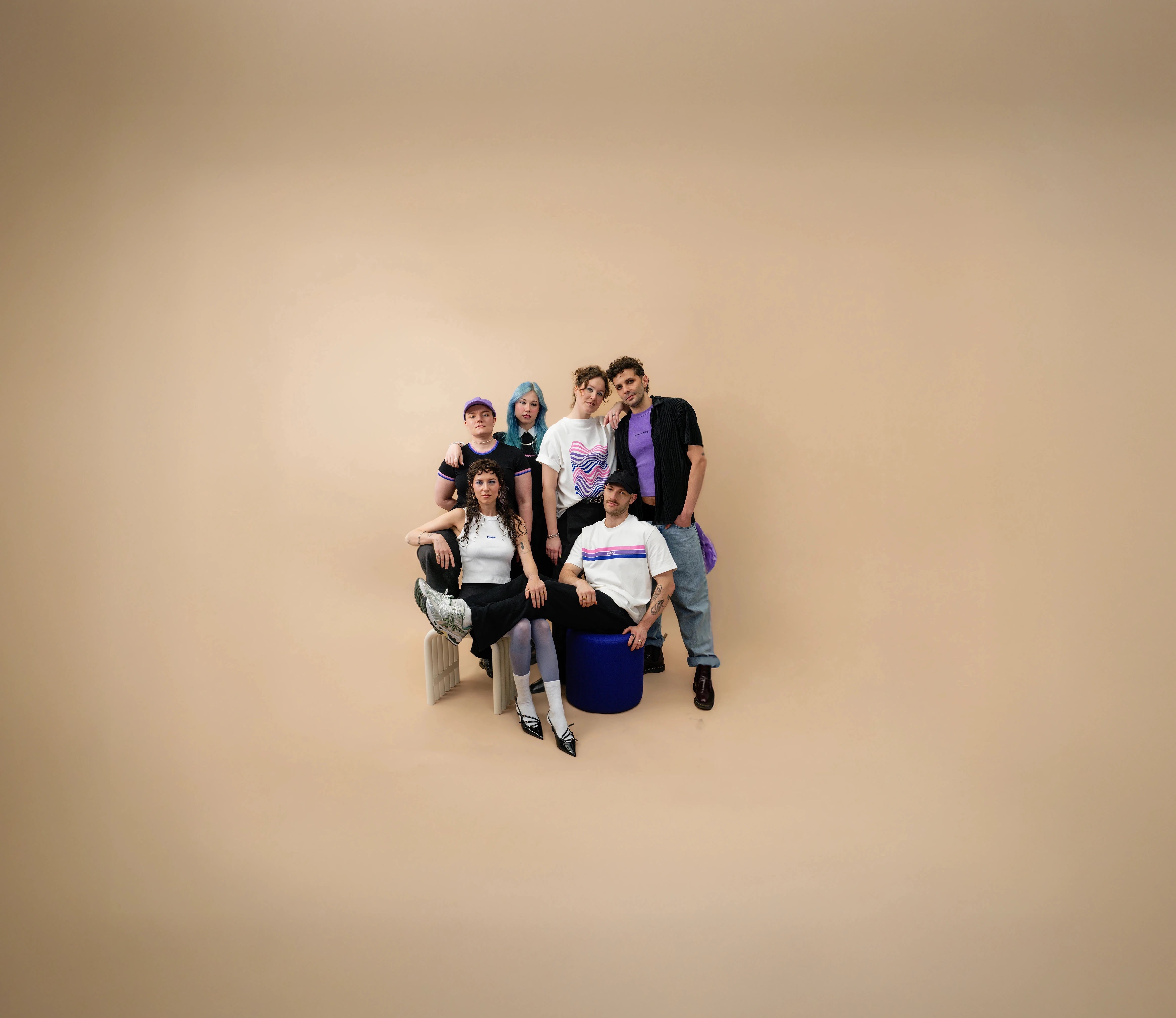 Group of diverse models wearing Biweekly clothing with graphic prints and bi pride color accents, posing together against a beige background