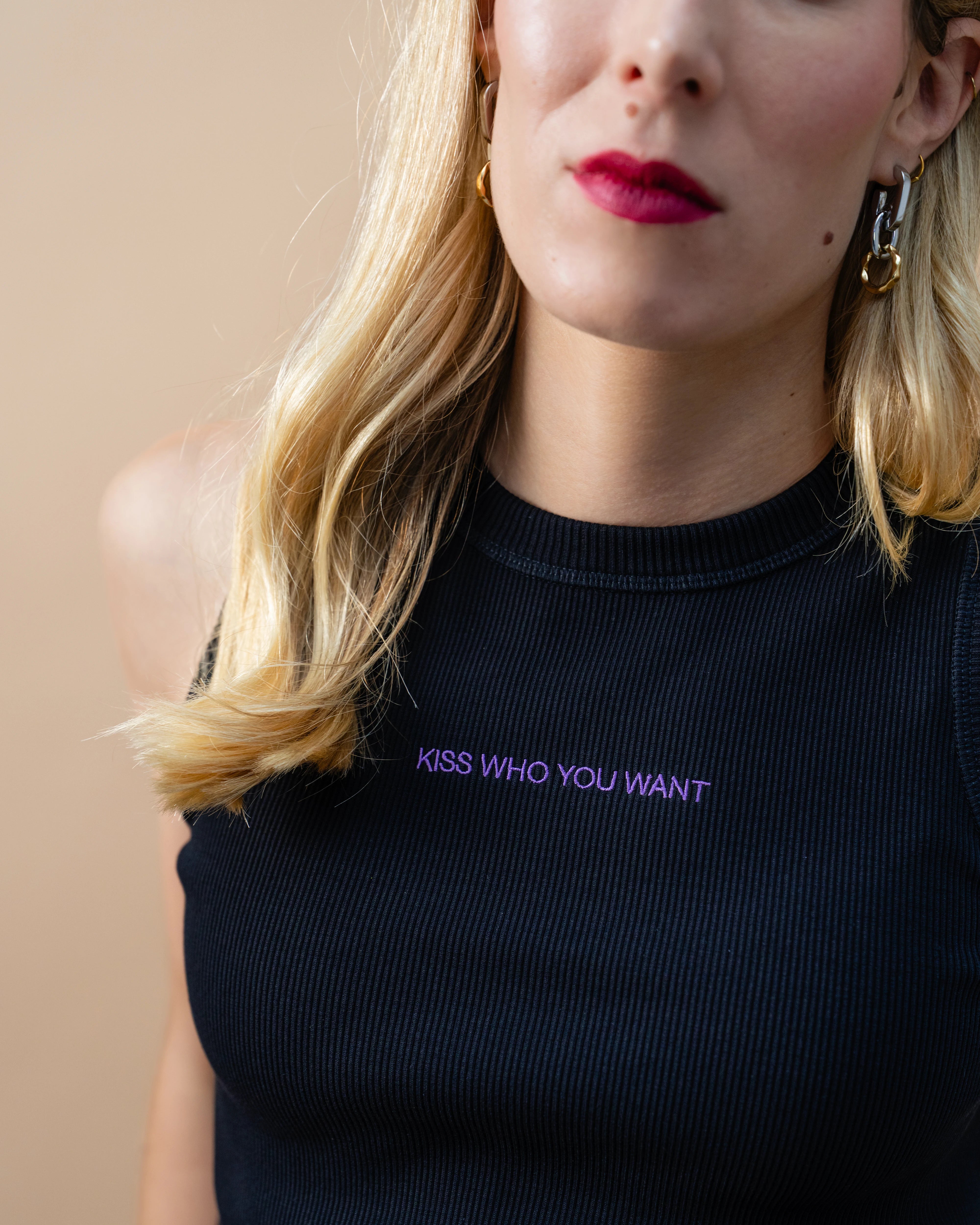 Detail view of a black Biweekly tank top with lilac ‘Kiss Who You Want’ text against beige background