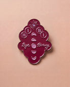 Burgundy Biweekly pin with 'Hi Bi - Bye Binary' text and moon phase illustration, flatlay against a beige background