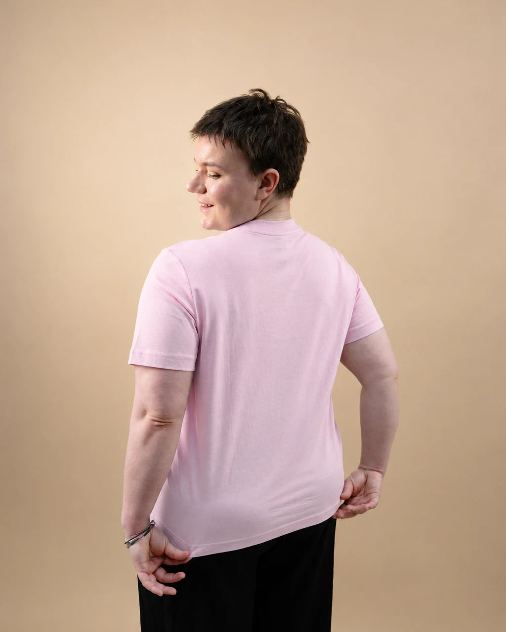 Model wearing light pink Biweekly T-shirt, back view, against beige background