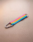 Keychain in pan pride flag colors with silver carabiner and blue yarn laying on beige surface