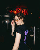 Model wearing an oversized black Biweekly T-shirt with a moon phase print that has gradient bi pride colours, back view in a club setting