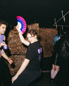 Model wearing an oversized black Biweekly T-shirt with a moon phase print that has gradient bi pride colours, back view dancing in a club setting