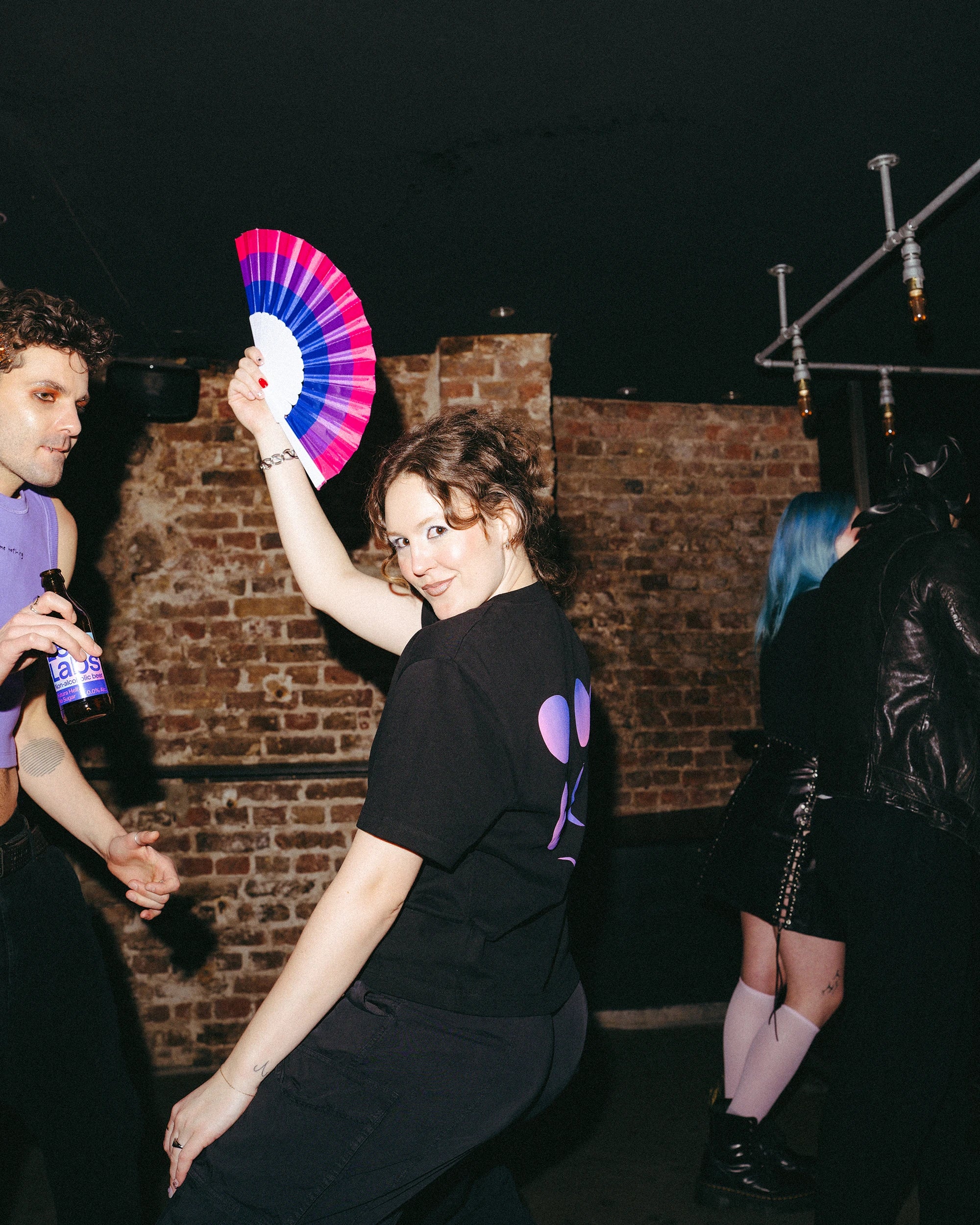 Model wearing an oversized black Biweekly T-shirt with a moon phase print that has gradient bi pride colours, back view dancing in a club setting