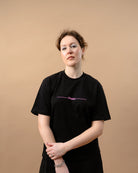 Model wears an oversized black Biweekly T-shirt with pink text 'Phase' crossed out by a long line, front view against a beige background