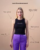 Model wearing a black Biweekly tank top with white ‘Bi, actually’ text, front view against a beige background. Text that gives information about top. 