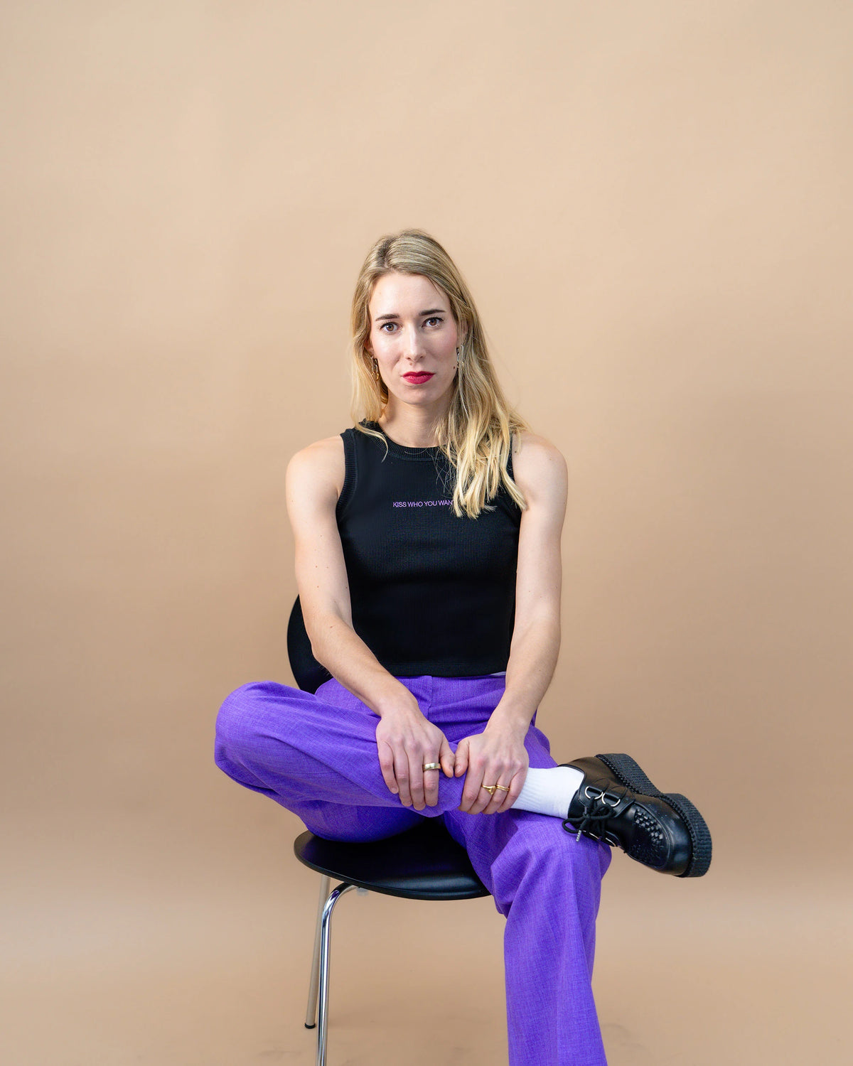 Founder Lea Mishra sitting on a chair looking in the camera holding her leg against beige background