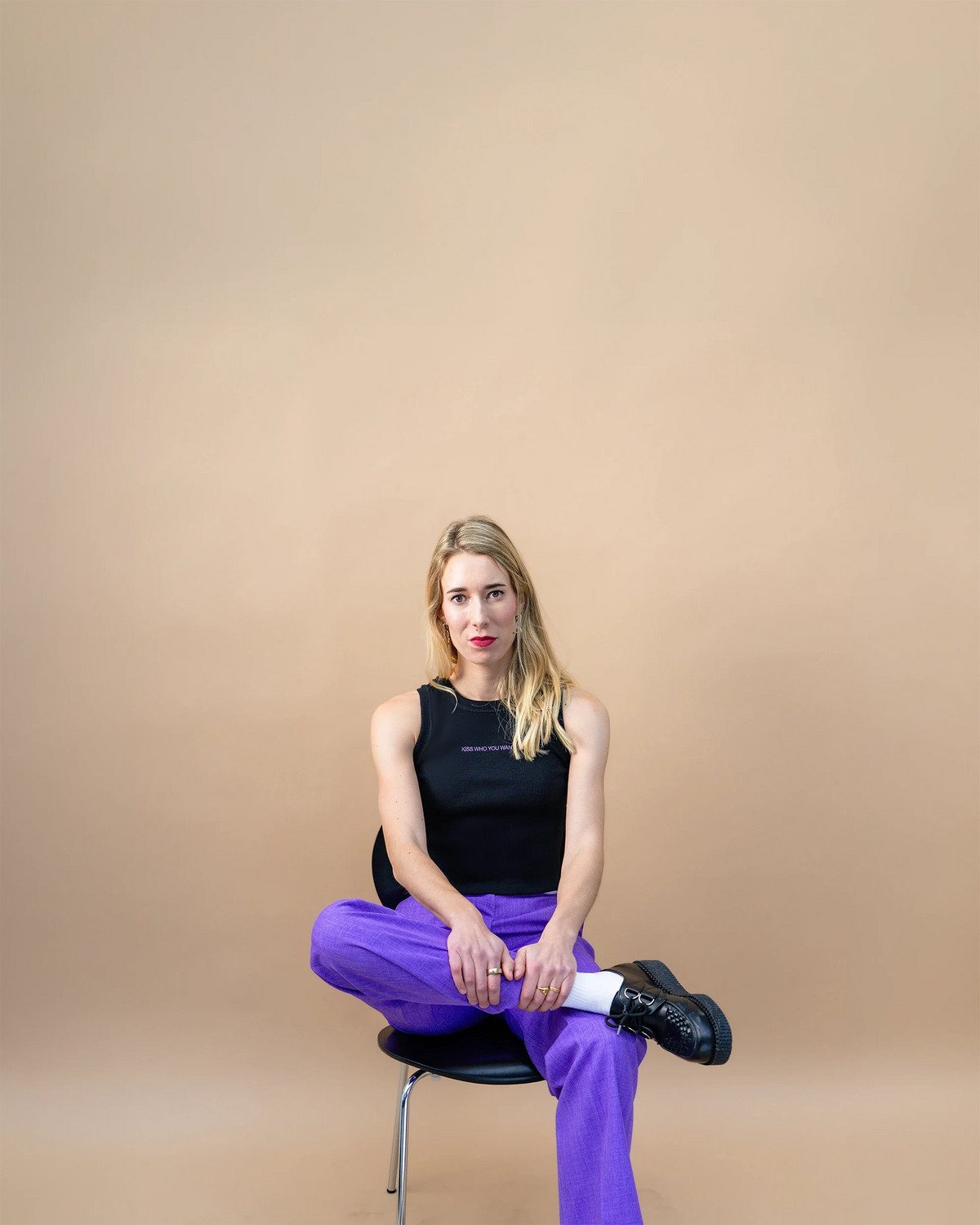 Founder Lea Mishra sitting on a chair looking in the camera holding her leg against beige background
