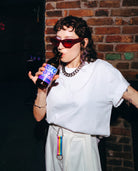 Model wears Biweekly keychain in pan pride flag colors with silver carabiner and blue yarn on skirt loops while drinking in a club scenario
