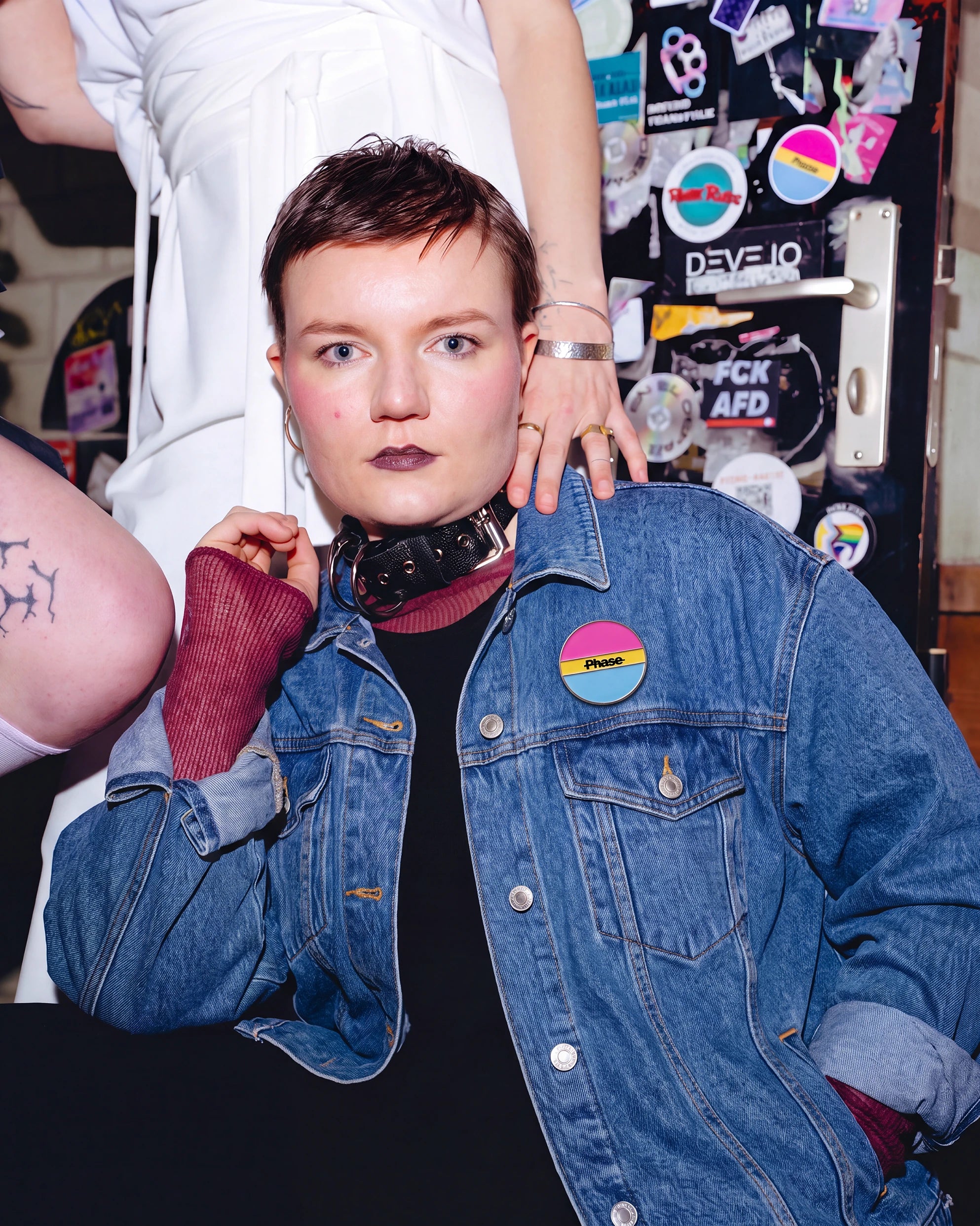 Model is wearing Biweekly Pin in pan colours with a crossed out 'Phase' text on a jeans jacket