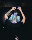 Model wearing a black Biweekly cap with bi pride flag strap and ‘Kiss Who You Want’ text on the back, back view, in a club scenario, dancing