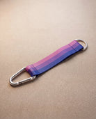 Keychain in bi pride flag colors with silver carabiner and blue yarn laying on beige surface