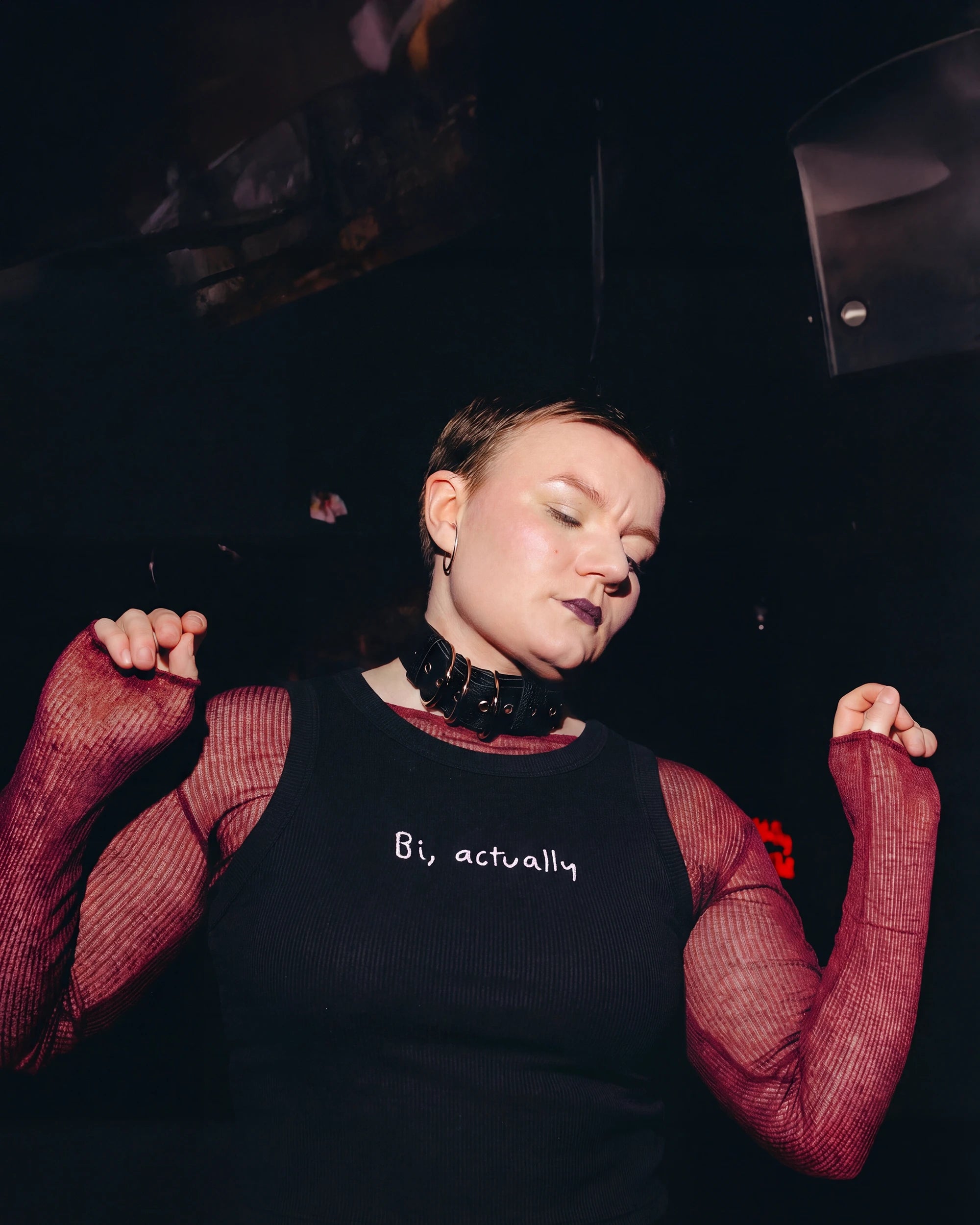 Model wearing a black Biweekly tank top with white ‘Bi, actually’ text, front view dancing in a club scene