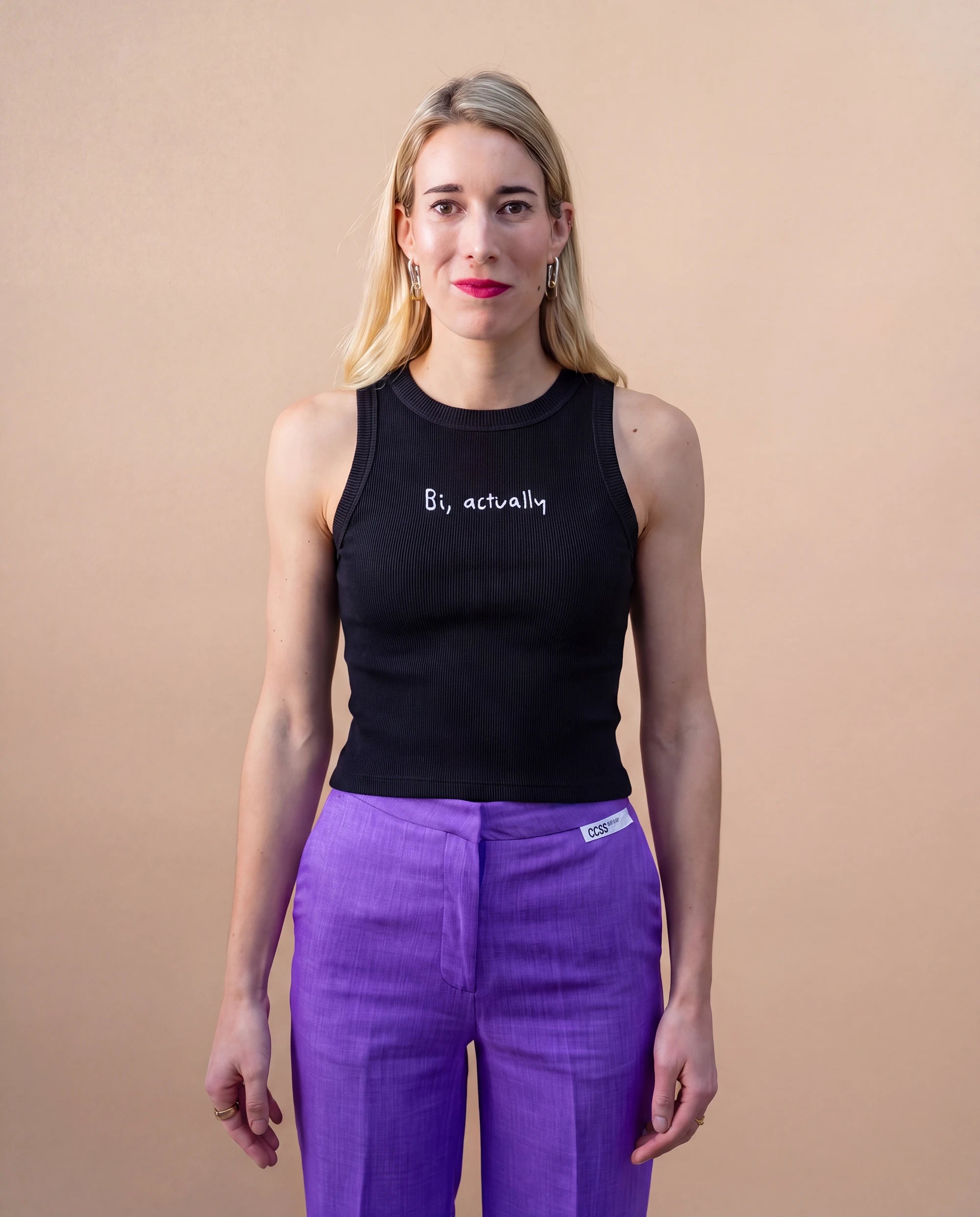 Model wearing a black Biweekly tank top with white ‘Bi, actually’ text, front view against a beige background
