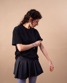 Model wears an oversized black Biweekly T-shirt with black ‘BiBi’ logo, front view against a beige background. Model is adjusting her sleeve.